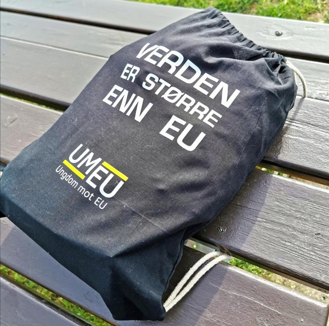 En svart ungdom mot EU gymbag, ligger på en grå benk. Baggen har påskriften verden er større enn EU, og har hvit snor. I bakgrunnen er gresset grønt.